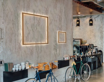 May include: Two bicycles parked in front of a cafe with a concrete wall. The cafe has a black counter and shelves with various items. The wall has two framed pictures.