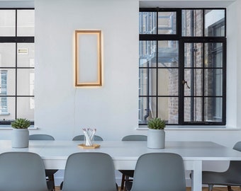 May include: A white table with six gray chairs, a potted plant, and a framed picture on a white wall. The table is set with a vase of pencils and a wooden tray.