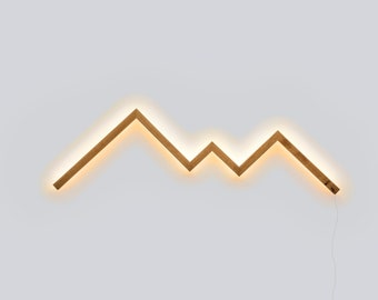 May include: A wooden wall light shaped like a mountain range with a warm white LED light strip. The light is mounted on a white wall.