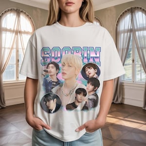 May include: White t-shirt featuring a retro design with the name "SOOBIN" in a teal and pink gradient. The shirt includes multiple circular portraits of a male musical artist. The overall design has a vintage aesthetic.