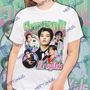 Puede incluir: Camiseta blanca con un gr&aacute;fico de la banda Stray Kids. El dise&ntilde;o presenta el texto "Seungmin" en verde y rosa, y m&uacute;ltiples im&aacute;genes de los miembros de la banda en un estilo vintage.