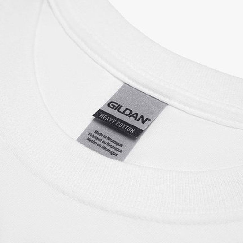 May include: Close-up of a white t-shirt collar with a gray tag. The tag reads "GILDAN HEAVY COTTON" and includes text indicating the shirt was made in Nicaragua in English, French, and Spanish.