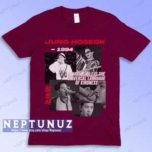 May include: Burgundy t-shirt featuring a collage of images and text. The text includes "JUNG HOSEOK - 1994" and "A WARM SMILE IS THE UNIVERSAL LANGUAGE OF KINDNESS." The shirt also has the shop's name and website address.