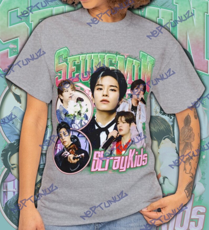 Puede incluir: Una camiseta gris con un collage de im&aacute;genes de un artista musical, con el nombre "SEUNGMIN" en letras verdes y rosas. Las palabras "Stray Kids" est&aacute;n impresas en rosa debajo de las im&aacute;genes. La camiseta tiene un dise&ntilde;o vintage y retro.