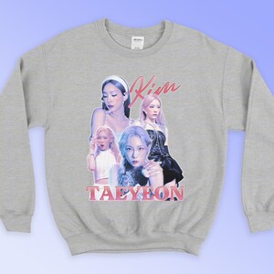 K&ouml;nnte beinhalten: Ein hellgraues Sweatshirt mit einer Collage von Bildern einer Frau, mit dem Namen "Kim" in rosa Schrift &uuml;ber den Bildern und dem Namen "Taeyeon" in rosa Blockbuchstaben darunter. Das Sweatshirt hat lange &Auml;rmel.