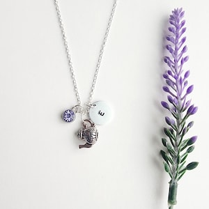 May include: Silver necklace with a charm of a teapot, a small purple crystal, and a silver disc with the letter "E" on it.