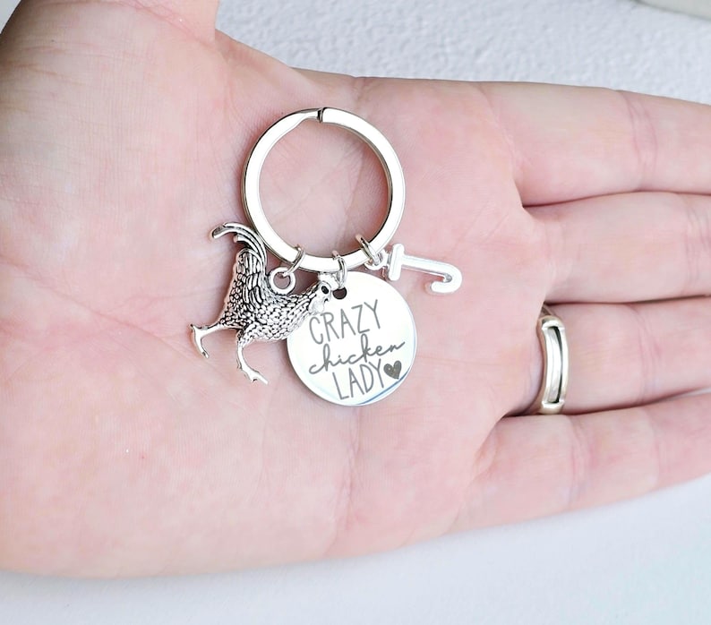 May include: Silver-toned keychain featuring a rooster charm and a round tag. The tag reads "Crazy Chicken Lady" with a heart symbol. The keychain is held in a hand.