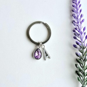May include: A silver keychain with a purple crystal charm and a silver letter A charm.