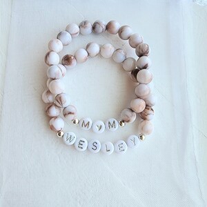 May include: Two white and brown marble bead bracelets with gold letter beads spelling "MOM" and "WESLEY".