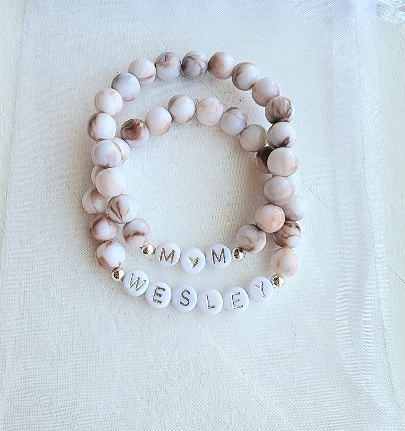 May include: Two white and brown marble bead bracelets with gold letter beads spelling "MOM" and "WESLEY".