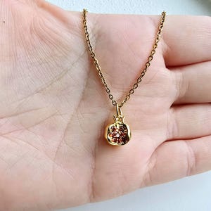 K&ouml;nnte beinhalten: Eine goldene Kettenkette mit einem Granatapfel-Anh&auml;nger. Der Anh&auml;nger ist aus Gold und hat rote Edelsteine.
