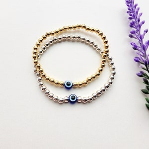 May include: Two beaded bracelets with evil eye charms. One bracelet is gold and the other is silver.
