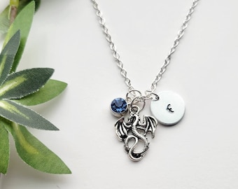 May include: Silver necklace with a dragon charm, a blue crystal, and a silver disc with the letter 'E' on it.