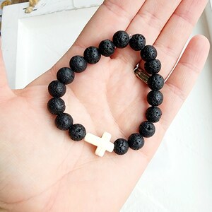 May include: Black lava rock beaded bracelet with a white cross charm.