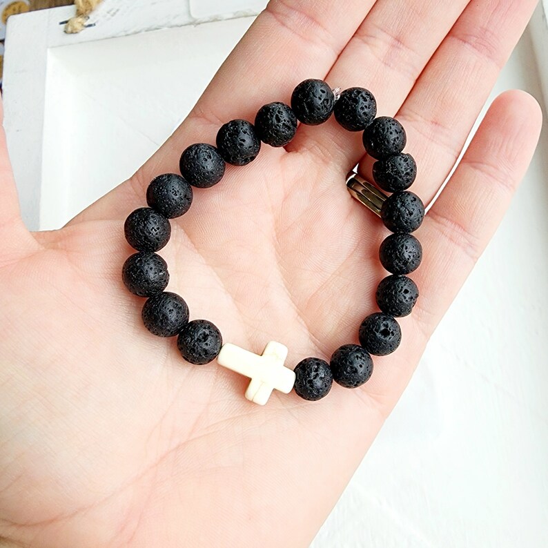 May include: Black lava rock beaded bracelet with a white cross charm.