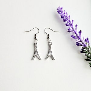 May include: A pair of silver earrings with a small Eiffel Tower charm adorned with clear rhinestones.