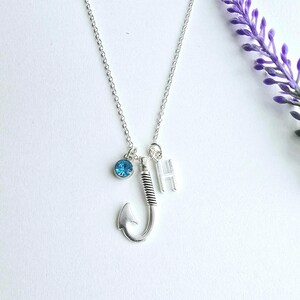 May include: A silver necklace with a fishing hook charm, a blue crystal, and a silver letter 'H' charm.