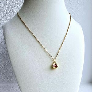 K&ouml;nnte beinhalten: Eine goldene Kettenkette mit einem kleinen, strukturierten, rot-goldenen Anh&auml;nger in Form eines Apfels.