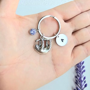 May include: A silver keychain with a sloth charm, a purple rhinestone, and a silver disc with the letter "A" engraved on it.