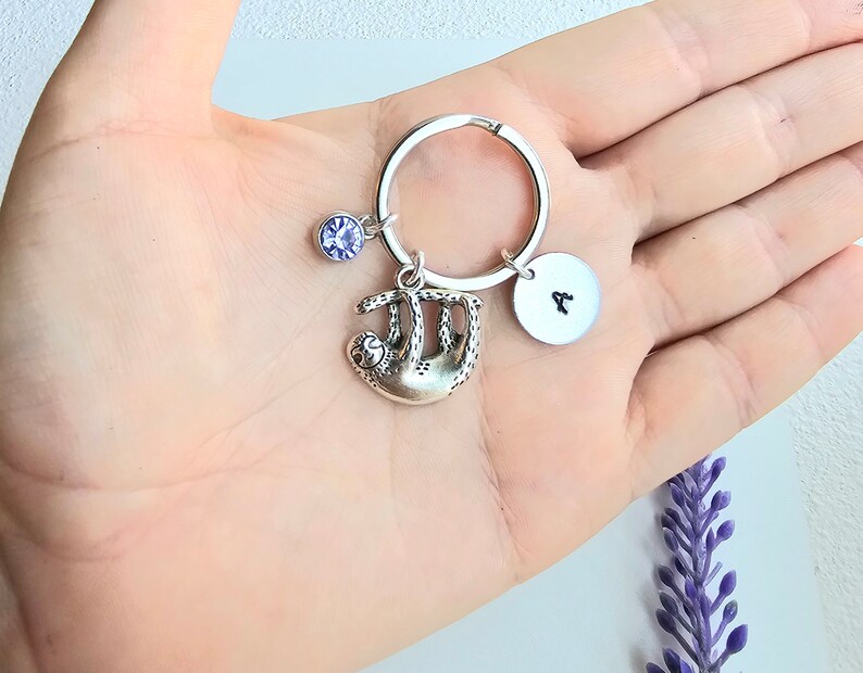 May include: A silver keychain with a sloth charm, a purple rhinestone, and a silver disc with the letter "A" engraved on it.