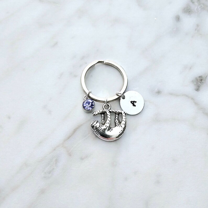 May include: Silver sloth keychain with a purple crystal charm and a silver disc charm with the letter "A" engraved on it.