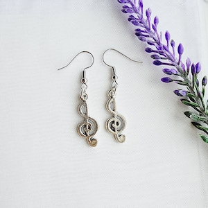 May include: A pair of silver earrings with a treble clef design. The earrings are hanging from a white background.