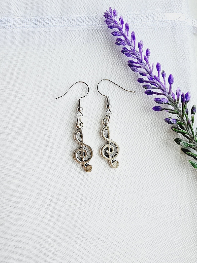 May include: A pair of silver earrings with a treble clef design. The earrings are hanging from a white background.
