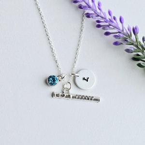 May include: A silver necklace with a flute charm, a small blue crystal charm, and a silver charm with the letter "L" on it.