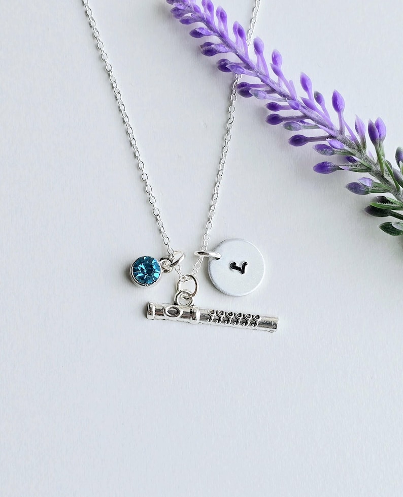 May include: A silver necklace with a flute charm, a small blue crystal charm, and a silver charm with the letter "L" on it.