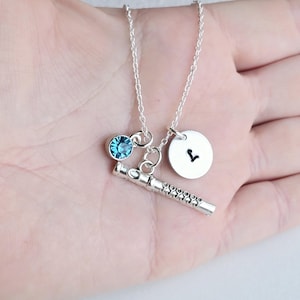 May include: Silver necklace with a blue crystal charm, a flute charm, and a silver charm with the letter V.