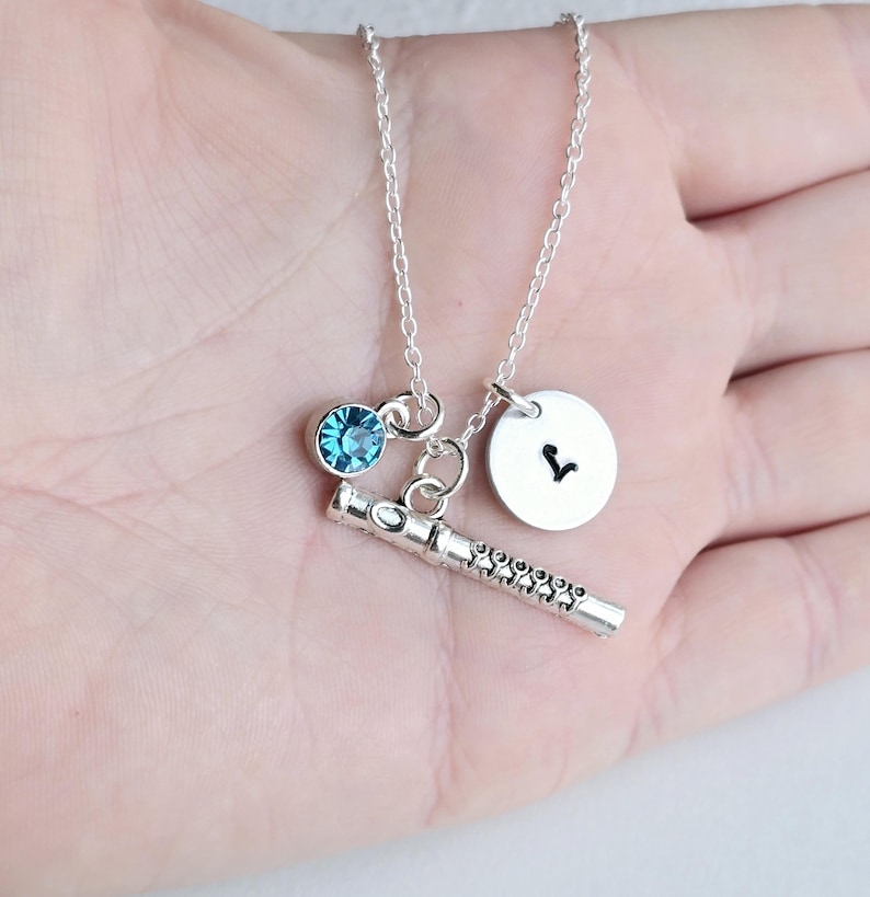 May include: Silver necklace with a blue crystal charm, a flute charm, and a silver charm with the letter V.