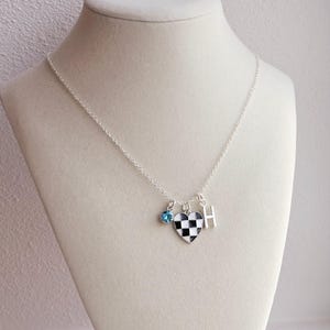 May include: A silver chain necklace with a checkerboard heart charm, a small blue crystal charm, and a silver charm with the letter "H".