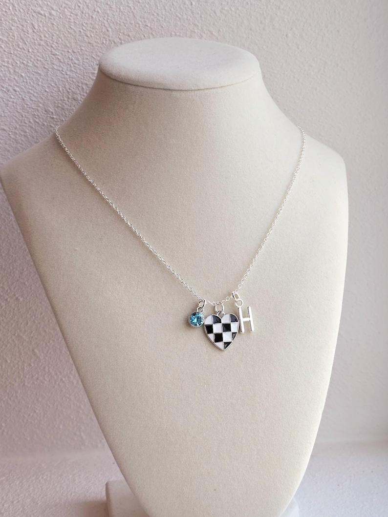 May include: A silver chain necklace with a checkerboard heart charm, a small blue crystal charm, and a silver charm with the letter "H".
