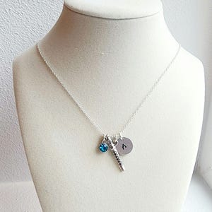 May include: A silver necklace with a small blue crystal charm, a silver charm shaped like a flute, and a silver disc charm with the letter "A" engraved on it.