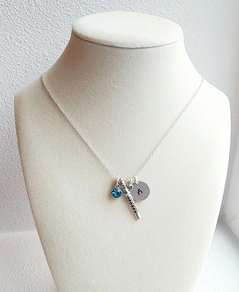 May include: A silver necklace with a small blue crystal charm, a silver charm shaped like a flute, and a silver disc charm with the letter "A" engraved on it.