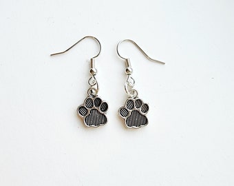 May include: A pair of silver dangle earrings with a black paw print charm.