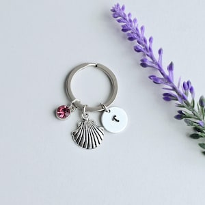 May include: Silver key chain with a pink rhinestone, a seashell charm, and a round charm with the letter "T" on it.