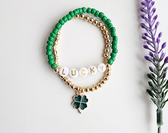 May include: A green and gold beaded bracelet with a four-leaf clover charm and the word "LUCKY" spelled out in white beads.