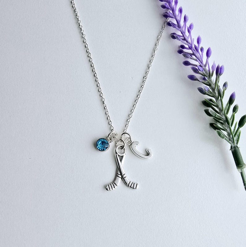 Puede incluir: Un collar de plata con un dije de cristal azul, un dije de palo de hockey y un dije con la letra "C".