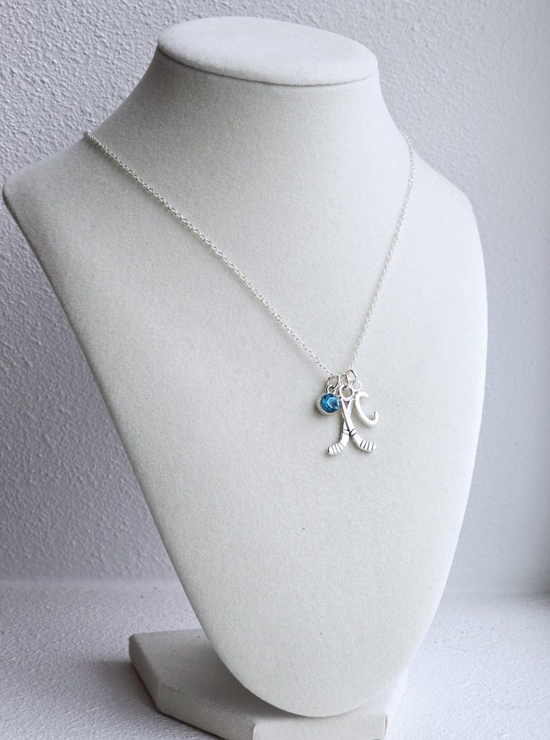 Puede incluir: Un collar de plata con un dije de cristal azul, un dije de palo de hockey y un dije con la letra "C".