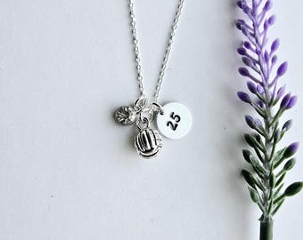 May include: Silver necklace with a volleyball charm, a small flower charm, and a round charm with the number 25.