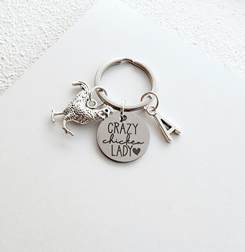 May include: Silver-toned keychain featuring a chicken charm, a circular pendant with the text "Crazy Chicken Lady" and a heart, and a letter "A" charm. The keychain is on a silver ring, and the background is white.