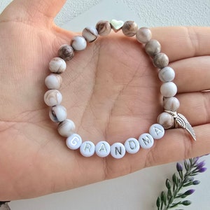 Puede incluir: Pulsera de cuentas blancas con cuentas marmoleadas marrones, un dije de coraz&oacute;n plateado y un dije de ala de &aacute;ngel plateado. La pulsera tiene la palabra "GRANDMA" escrita en letras plateadas sobre cuentas blancas.