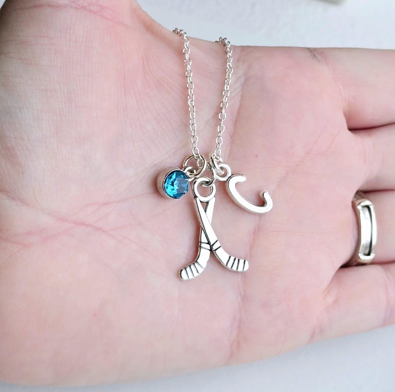 Puede incluir: Collar de plata con un dije de cristal azul, un dije de palo de hockey y un dije con la letra C.