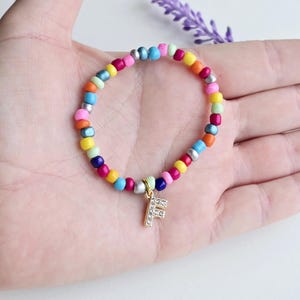 May include: A colorful beaded bracelet with a gold charm featuring the letter 'F' adorned with clear rhinestones.
