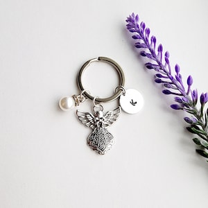 May include: Silver angel charm keychain with a pearl bead and a silver disc with the letter K engraved on it.