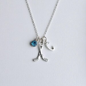 Puede incluir: Un collar de plata con un dije de cristal azul, un dije de palo de hockey de plata y un dije de letra C de plata.
