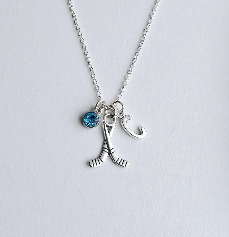 Puede incluir: Un collar de plata con un dije de cristal azul, un dije de palo de hockey de plata y un dije de letra C de plata.