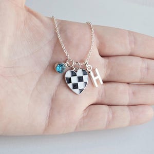 May include: A silver necklace with a checkerboard heart charm, a blue gemstone charm, and a silver letter 'H' charm.