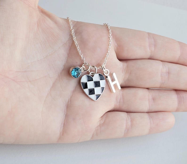 May include: A silver necklace with a checkerboard heart charm, a blue gemstone charm, and a silver letter 'H' charm.